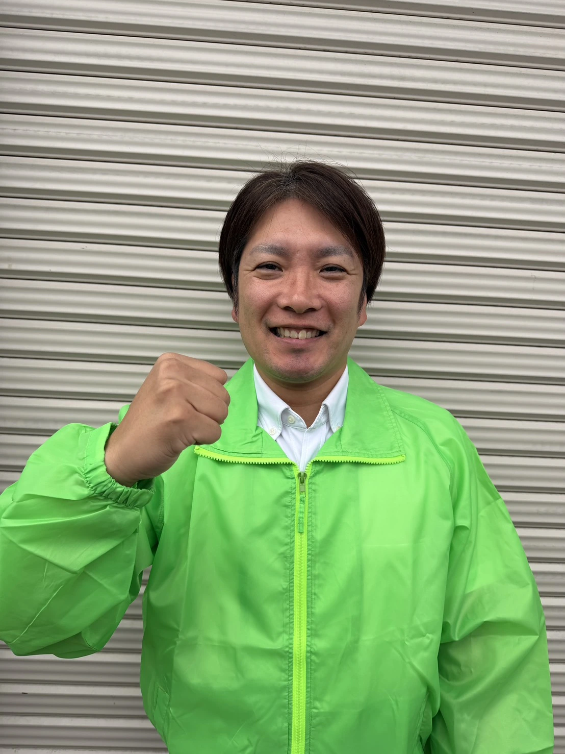 電話を使わない相談の相談案内に添えた、緑色の上着を着てシャッターの前で片手を上げた人物